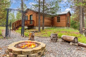 A log cabin with a fire pit, wooden deck, and a metal gate.