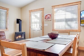 Un coin repas avec une table en bois, des chaises, un saladier et un poêle à bois.