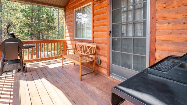 Une cabane en bois avec une véranda, un barbecue et un banc.