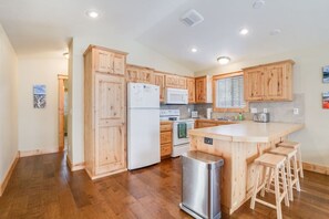 Une cuisine moderne avec des meubles en bois, un îlot central doté de tabourets, des appareils en acier inoxydable et une vue sur l’extérieur.