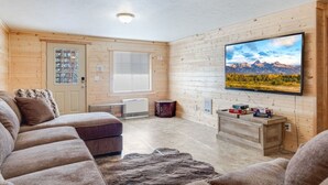 L’intérieur d’un chalet confortable, avec une grande télévision, un canapé et un tapis rustique.