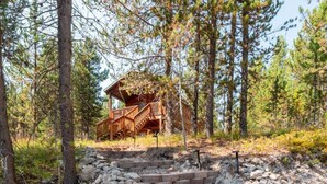 Une cabane dotée d’une terrasse en bois et d’un escalier menant à celle-ci, le tout entouré d’arbres.