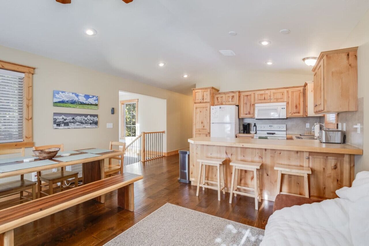 A spacious kitchen with wooden cabinets and a central island, a dining area with a bench and table, and a view of the outdoors through a window.