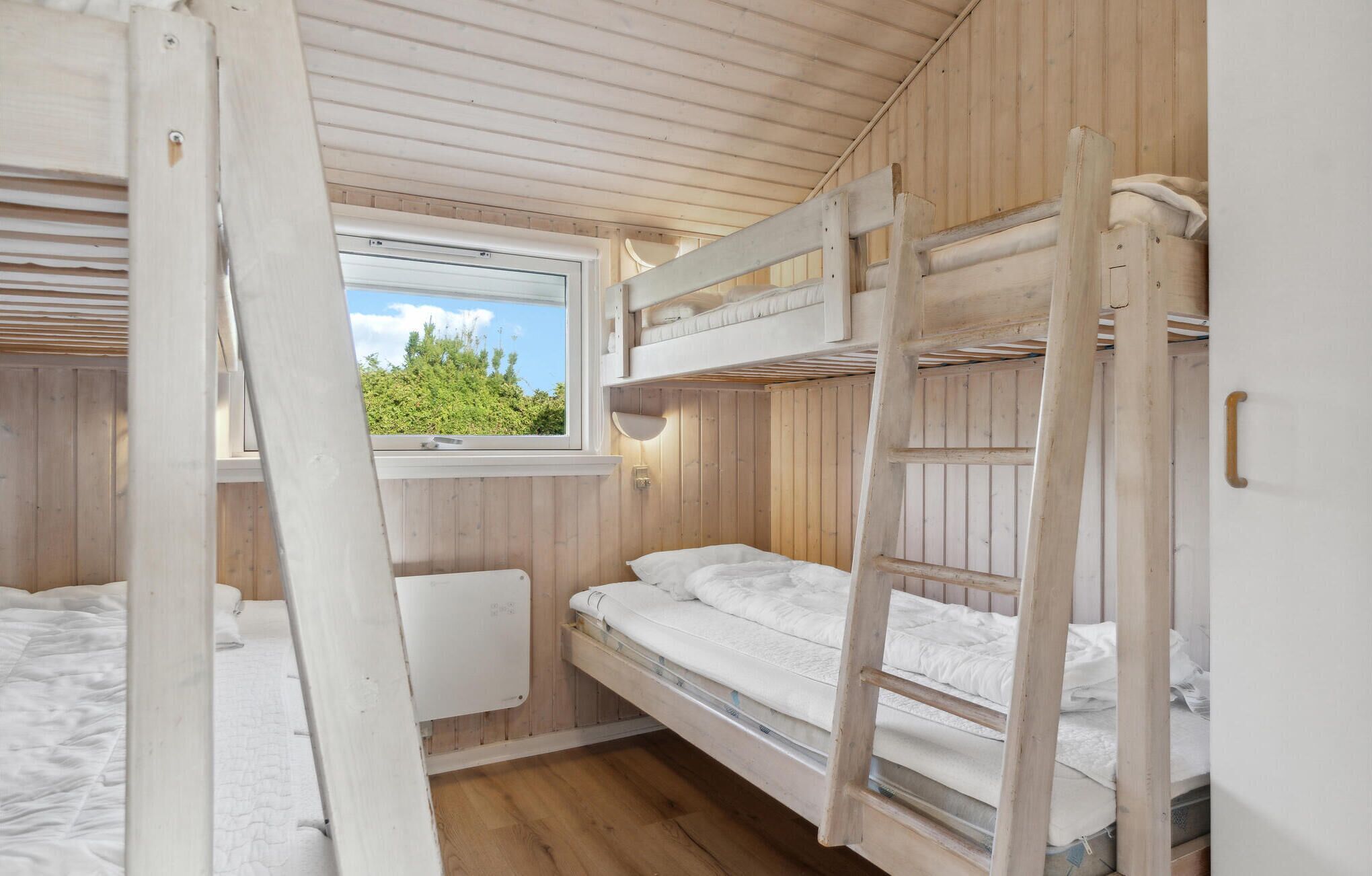 Dormitorio con literas, ventana, paredes de madera y colcha blanca.