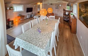 Een eetgedeelte met een lange tafel, bedekt met een bloemrijk tafelkleed, omringd door witte stoelen.