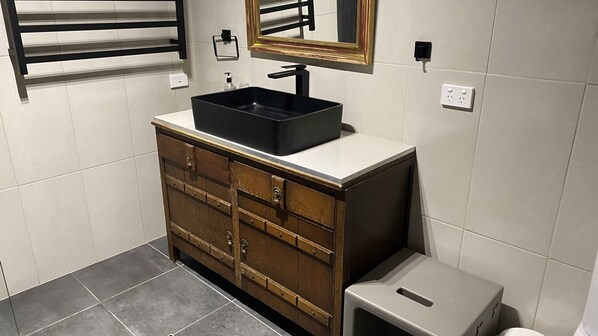 Ein Badezimmer mit einem schwarzen Waschbecken, einem Holzschrank und einer kleinen Mülleimer.