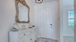 A hallway with a white door, a decorative mirror, a white cabinet with jars, and a patterned rug. - The Cape Escape - New Heated Saltwater Pool.  Just 10 minutes from Matlacha. (Cape Coral)