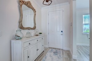 A hallway with a white door, a decorative mirror, a white cabinet with jars, and a patterned rug. - The Cape Escape - New Heated Saltwater Pool. Just 10 minutes from Matlacha. (Cape Coral)