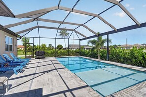 A covered outdoor swimming pool with lounge chairs and a barbecue grill.