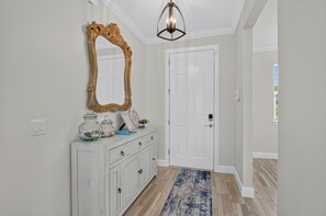 A hallway with a white door, a white console with drawers, a decorative mirror, and a blue rug.