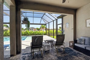 A sunroom with a view of a swimming pool, two chairs, a small table, and a couch.