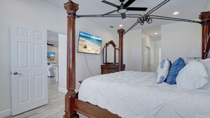 A bedroom with a four-poster bed, a ceiling fan, and a television on the wall. - The Cape Escape - New Heated Saltwater Pool.  Just 10 minutes from Matlacha. (Cape Coral)