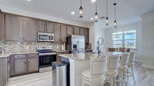 A modern kitchen with wooden cabinets, stainless steel appliances, and a central island with bar stools. - The Cape Escape - New Heated Saltwater Pool.  Just 10 minutes from Matlacha. (Cape Coral)