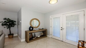 A hallway with a potted plant, a console table with decorative items, and a double door with frosted glass panels. - Impeccably maintained Marco Island oasis! (Marco Island)