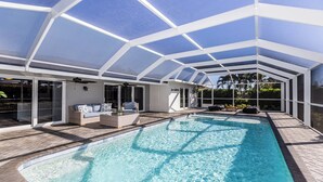 A covered swimming pool with a glass ceiling, a lounge area with a sofa and a coffee table, and a view of the surrounding greenery. - Impeccably maintained Marco Island oasis! (Marco Island)