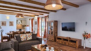 Una sala de estar acogedora con un sofá, una mesa de centro y un televisor. Se observa un aparador de madera y un comedor al fondo.