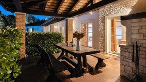 Un patio al aire libre con una mesa y bancos de madera, un jarrón con flores secas y un muro de piedra.