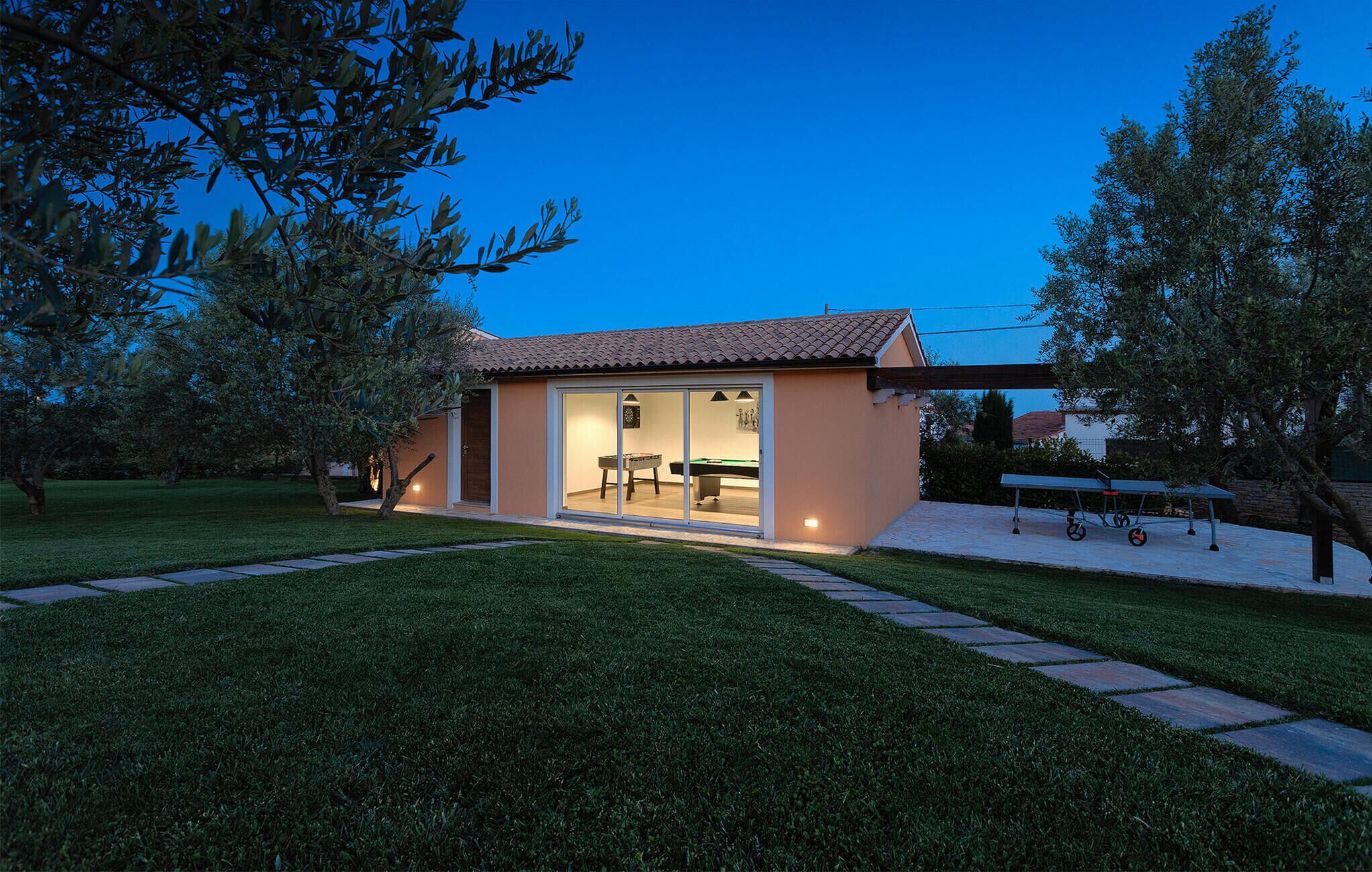 A small, single-story building with a tiled roof, a glass door entrance, and a visible pool table inside.