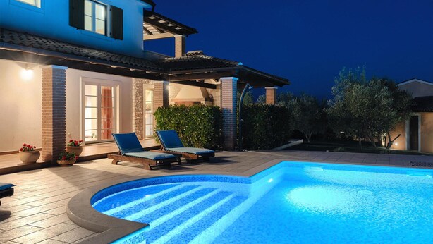 Una piscina de borde curvo, dos sillas de descanso y una zona de patio con pared de ladrillo y una ventana.