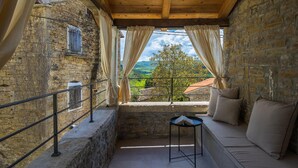 Un balcon accueillant avec des murs en pierre, un plafond en bois et une vue sur des collines verdoyantes.