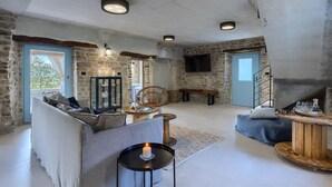 Un intérieur rustique avec des murs en pierre apparentes, une cheminée en pierre, un ensemble de canapés, une table à manger et un téléviseur fixé au mur.
