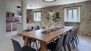 Un coin repas avec une table en bois et des chaises noires, une cuisine en arrière-plan et des murs en pierre.