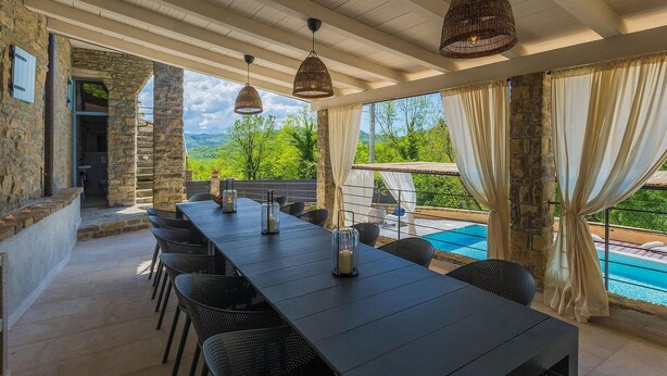 Une longue table à manger entourée de chaises, un luminaire suspendu et une vue sur une piscine.