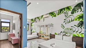 A modern hotel room with a large bed, a small seating area, and a wall mural with tropical leaves and the text "Moon coffee". - Rosemary Villa near Han River  (Da Nang)