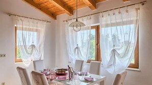 Un comedor con una mesa de vidrio, sillas blancas y cortinas traslúcidas.