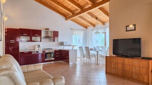 Una cocina moderna con armarios rojos, un comedor con mobiliario blanco, un sofá de cuero y un televisor sobre un mueble de madera.