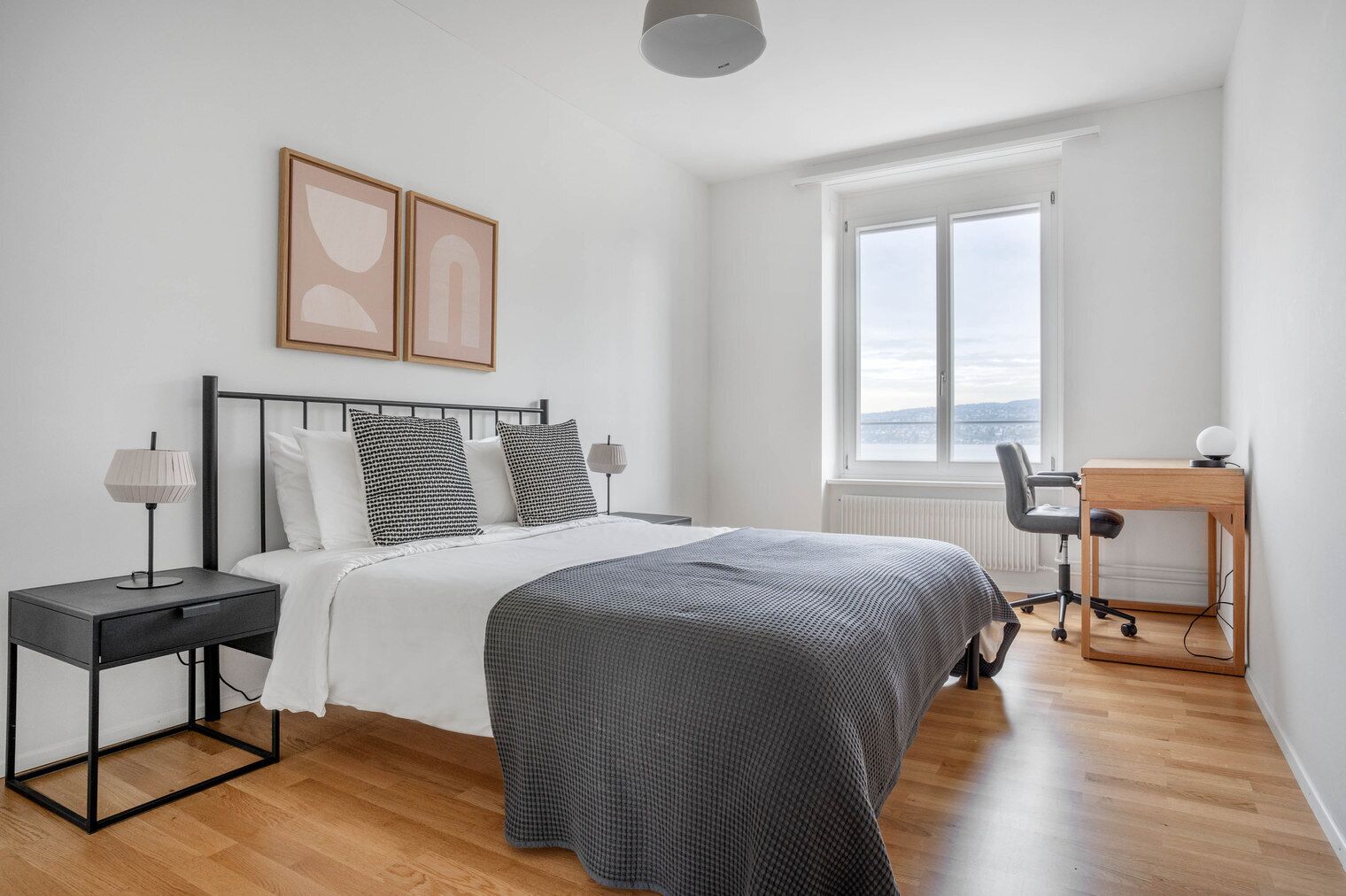 Un dormitorio moderno con cama, mesitas de noche, un escritorio y un ventanal amplio.