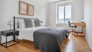 A modern bedroom with a bed, bedside tables, a desk, and a large window. - Chic Horgen 2BR w/ Storage Room & Lake View, nr Market, by Blueground (Zurich)