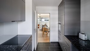 Ett modernt kök med mörka bänkskivor i granit, rostfria vitvaror och utsikt över en matplats med ett träbord och stolar.