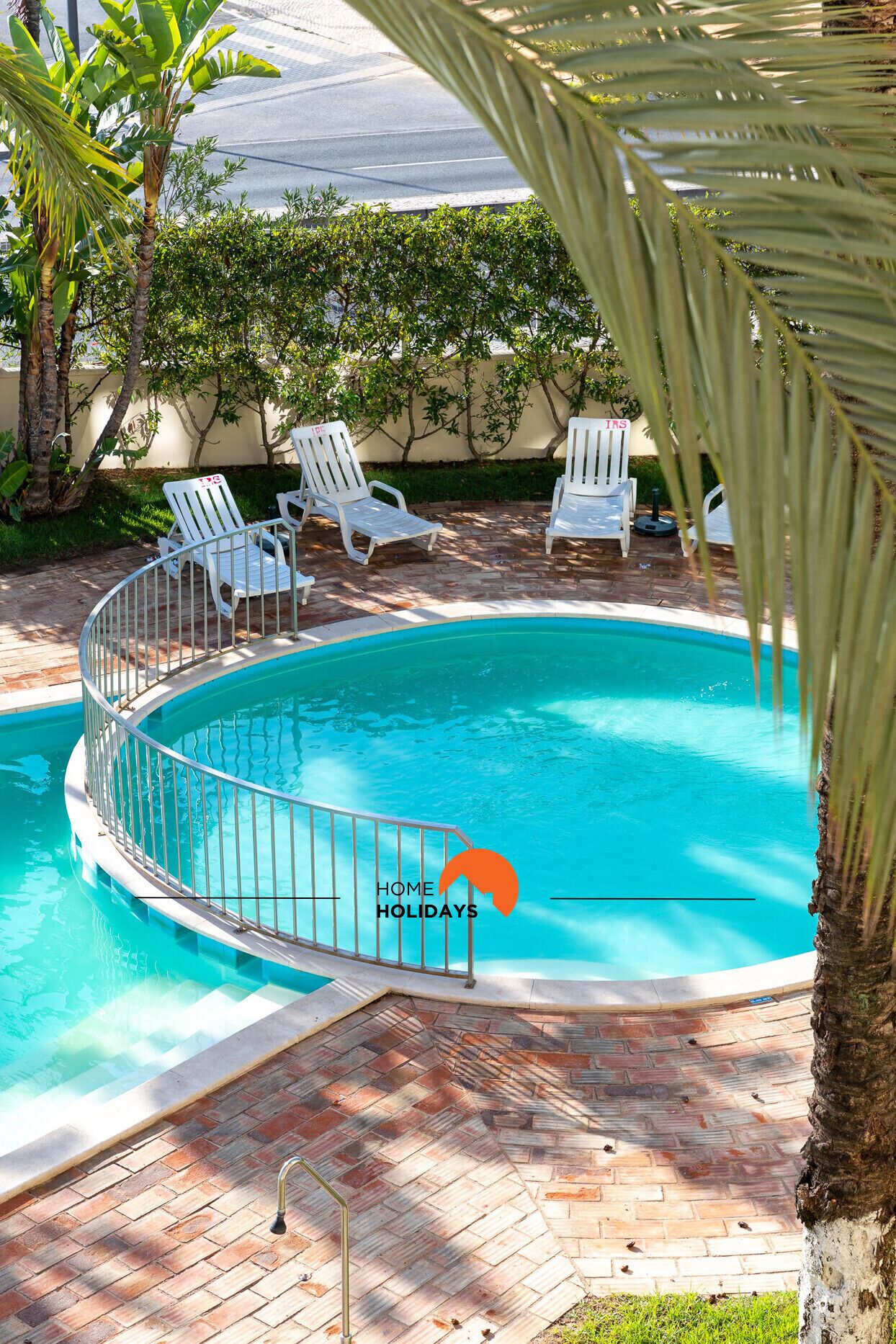 A circular pool with a metal railing, surrounded by white lounge chairs and palm trees.