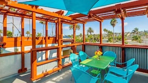 An outdoor patio with a table and chairs, a pergola structure, and a view of palm trees and buildings. - Discounted Rates - Ocean Beach Holiday (San Diego)
