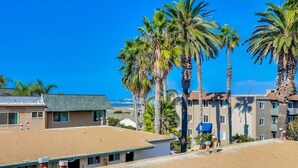 A hotel with multiple-story buildings, palm trees, and a clear blue sky. - Discounted Rates - Ocean Beach Holiday (San Diego)