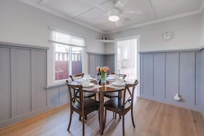 Une salle à manger avec une table ronde dressée pour quatre personnes, des chaises en bois, un vase de fleurs et une horloge au mur.