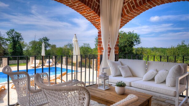 A covered outdoor seating area with wicker chairs and a white sofa, overlooking a swimming pool and lush greenery. - Beautiful home in Porec (Porec)