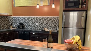 A kitchen with a central island, bar stools, a refrigerator, and a microwave.