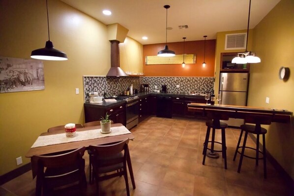 A kitchen with a dining area, featuring a central island, bar stools, and pendant lighting.