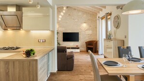 A modern kitchen with a built-in stove, a dining area with a wooden table and chairs, and a stone accent wall. - Amazing home in Motovun (Motovun)