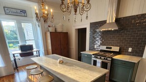 A modern kitchen with a central island, bar stools, a stove, and a microwave. - Take a trip back in time and stay at the Larissa House Inn! (Jacksonville)