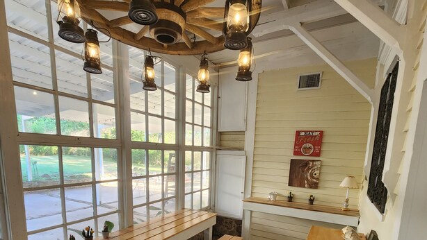A cozy room with wooden benches, a rustic ceiling, and a view of the outdoors through large windows. - Take a trip back in time and stay at the Larissa House Inn! (Jacksonville)