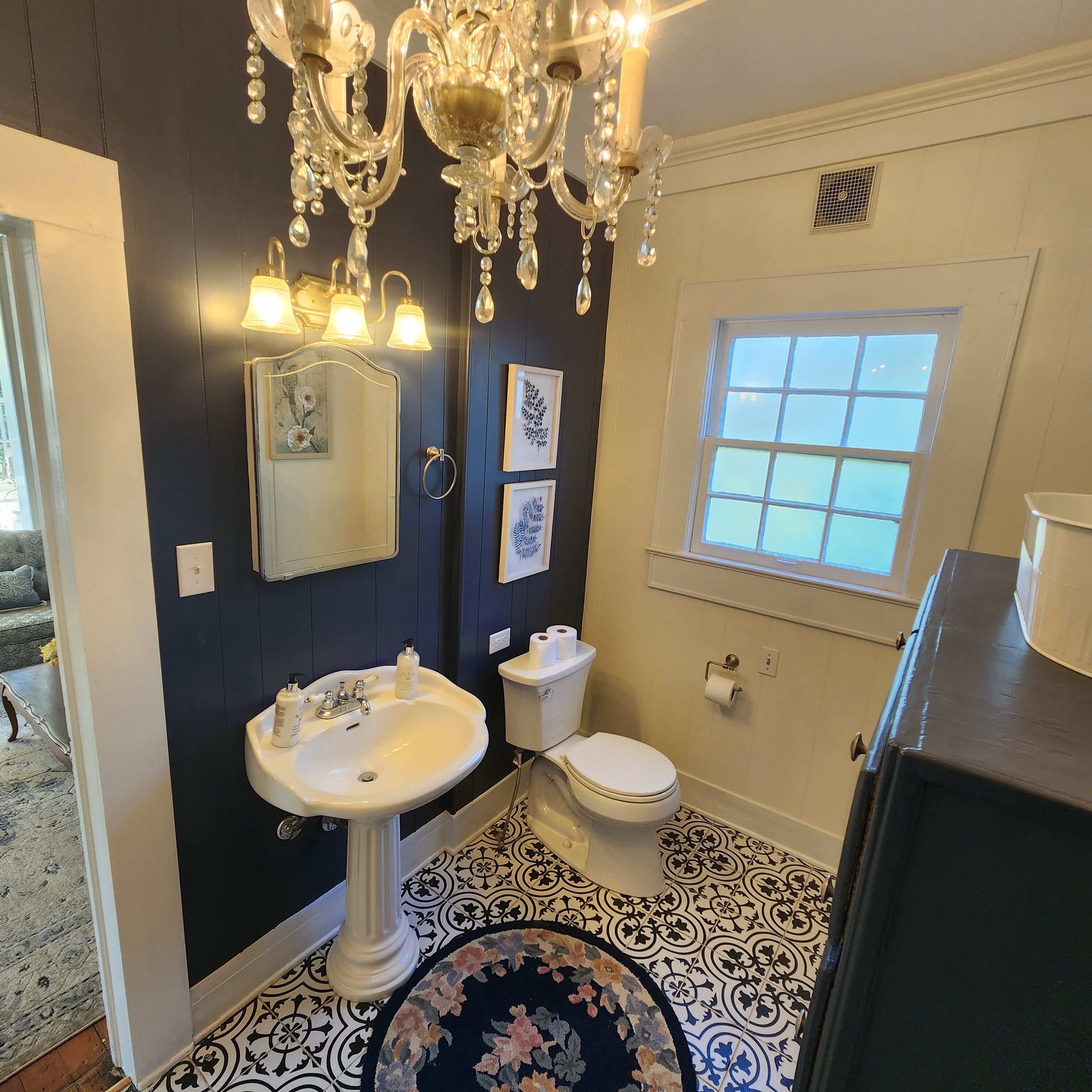A bathroom with a white sink, a toilet, a chandelier, and a window.