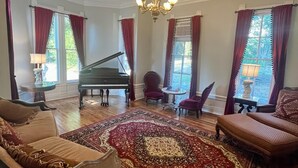A spacious living room with a grand piano, plush seating, and a large ornate rug. - Take a trip back in time and stay at the Larissa House Inn! (Jacksonville)