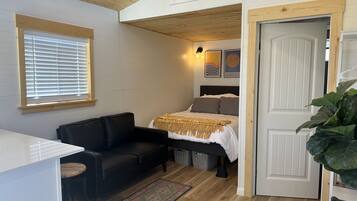 A compact room with a bed, a black leather sofa, a small table, and a large plant.