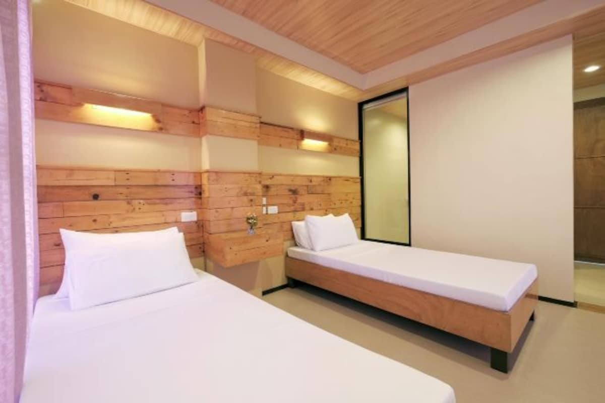 Una habitación de hotel moderna con dos camas individuales, cabeceros de madera y un espejo grande.