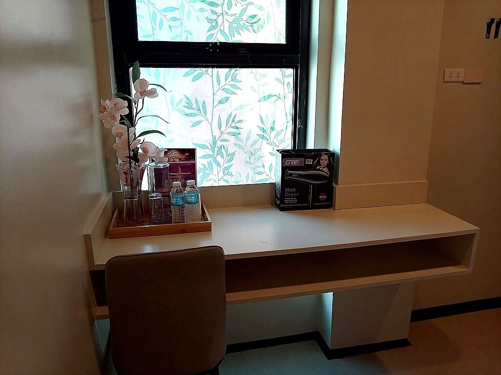 A desk with a window, a vase with flowers, and a hair dryer box.