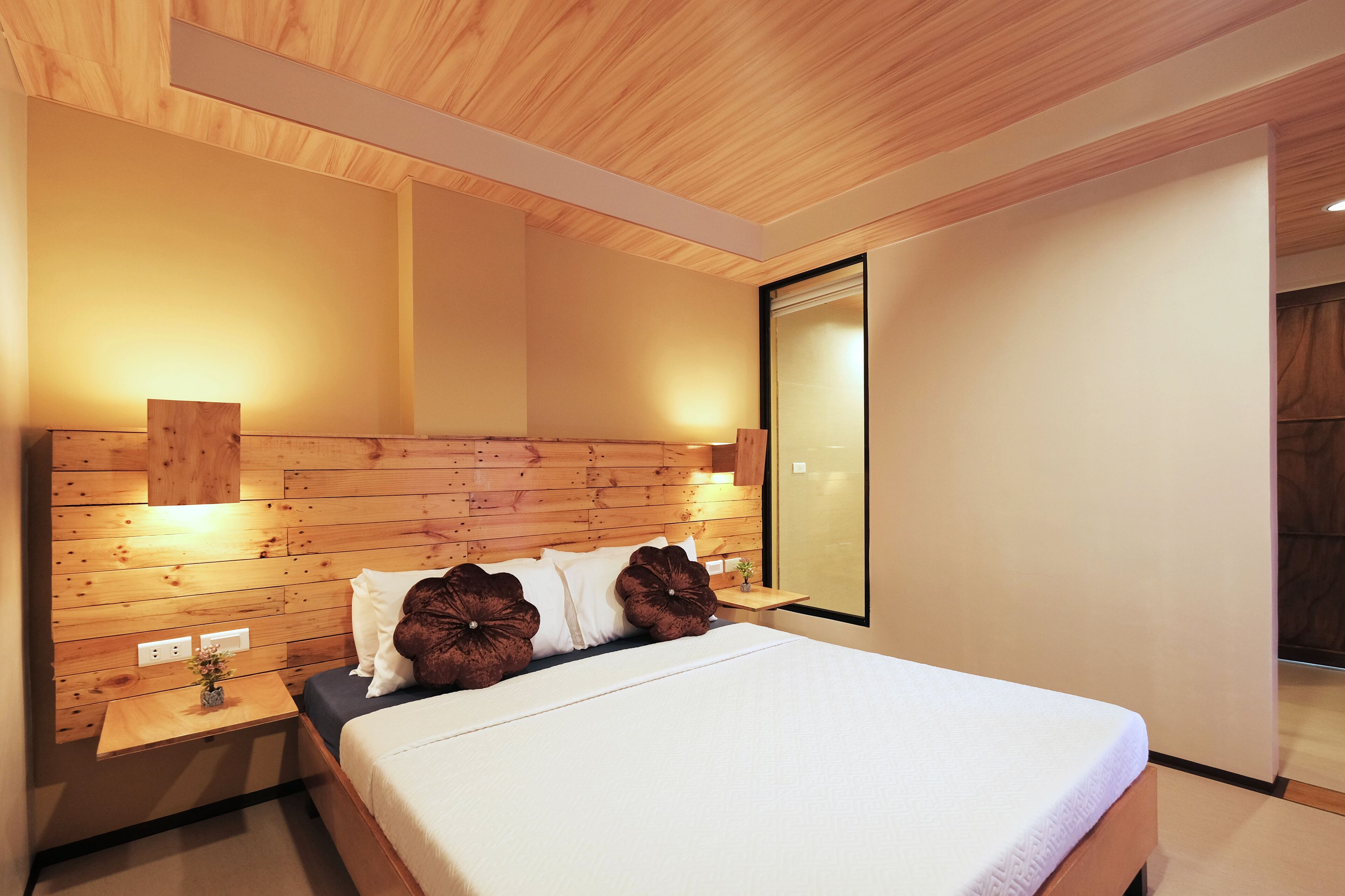 Ein modernes Schlafzimmer mit einem Holzkopfende, einem großen Bett mit weißer Bettwäsche und einem Nachttisch mit einer kleinen Pflanze.