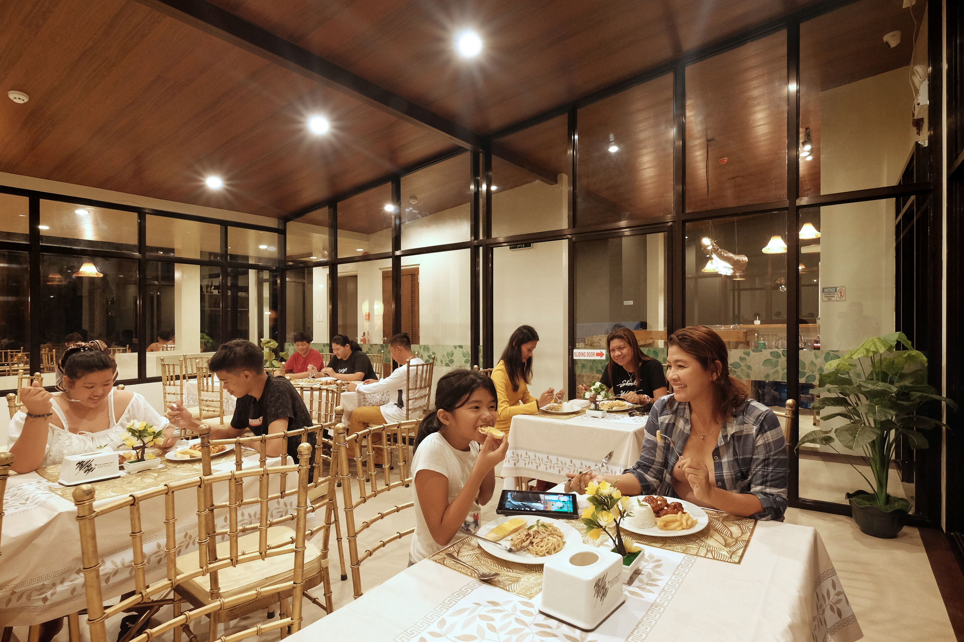 Comedor con mesas y sillas, techo de madera y ventanas amplias.